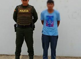 En la imagen se ve una persona detenida en custodia de un integrante de la Policía Nacional.
