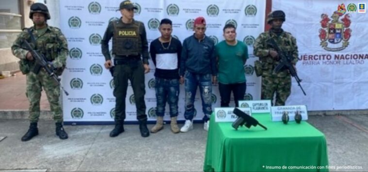 En la fotografía aparecen los tres capturados junto a un agente de la Policía Nacional y dos soldados del Ejército Nacional. En la parte posterior está una mesa con una subametralladora y dos granadas de fragmentación