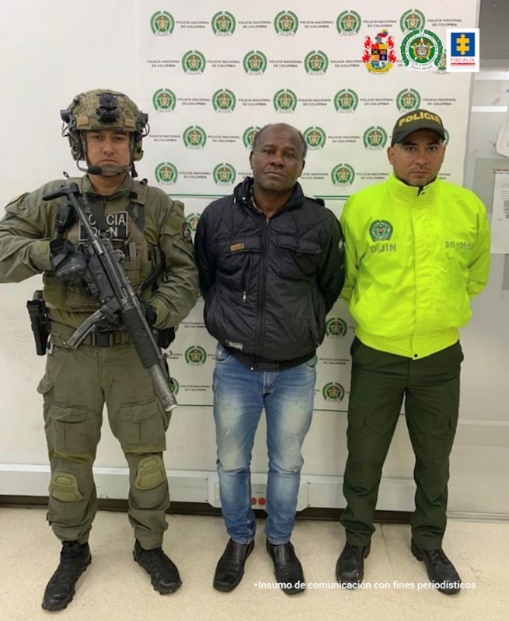 En la imagen se observa al hombre capturado vestido con uniformes de la policía nacional y del ejército.  En el reverso se encuentra la pancarta que identifica a la Policía Nacional.