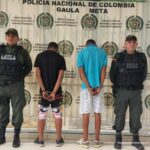 Los capturados están esposados con sus manos a la espalda, custodiados por dos uniformados de la policía nacional.