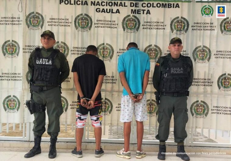 Los capturados están esposados con sus manos a la espalda, custodiados por dos uniformados de la policía nacional.