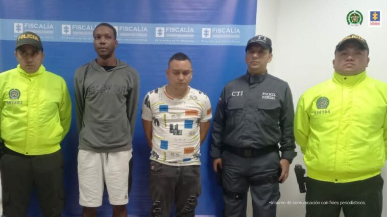 En la fotografía aparecen con los brazos atrás los dos presuntos implicados en el homicidio de una menor de edad. Uno de ellos es de tez negra y viste camiseta color gris de manga corta, bermudas claras y zapatillas blancas. El otro imputado es de tez  blanca y viste camiseta blanca con estampados de colores; jean gris oscuro con desgastes y zapatillas blancas. Al lado derecho de ellos hay un servidor del CTI de la Fiscalía y un uniformado de la Policía Nacional. Detrás de ellos hay un pendón institucional de la Fiscalía.