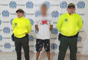 En la fotografía aparece un hombre capturado, acompañado de dos uniformados de la Policía. En la parte posterior un banner con logos de la entidad.