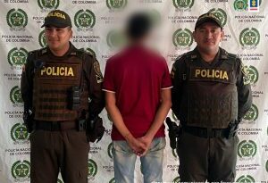 En la imagen aparece el capturado de espaldas junto a dos uniformados de la Policía Nacional. En la parte posterior se aprecia el banner que identifica a la Policía Nacional en Arauca