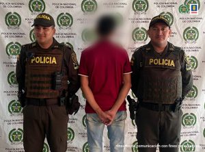 En la imagen aparece el capturado de espaldas junto a dos uniformados de la Policía Nacional. En la parte posterior se aprecia el banner que identifica a la Policía Nacional en Arauca