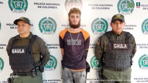 Se observa al capturado y a cada lado un funcionario de Policía Nacional. Atrás un pendón de Policía Nacional