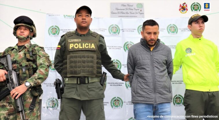 En la imagen se ve un detenido bajo custodia de la Policía y el Ejercito. Detrás suyo un backing de la Policía. 