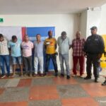 En la fotografía aparecen siete personas capturadas, acompañados de varios uniformados de la Policía y el Ejército Nacional. En la parte posterior un banner con el logo de la entidad y de la Fiscalía General de la Nación.