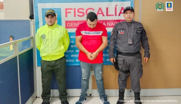 en la imagen se ve una persona detenida bajo custodia de un investigador del CTI y un Policía. Detrás suyo un backing de la Fiscalía.