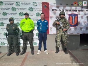 Se observa al capturado y a un costado uniformados de Policía Nacional y al otro del Ejército Nacional. Al fondo un pendón de Policía y otro de Ejército.