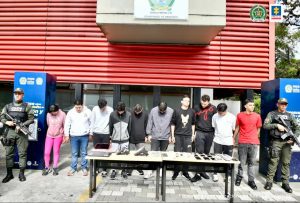 En la imagen se encuentra la mujer y los 9 hombres capturados con una mesa en al frente con celulares, armas de fuego y otros elementos incautados, y a los lados 2 servidores del Gaula de la Policía Nacional.