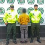 El hombre aparece de espalda a la cámara, está esposado con sus manos al frente y custodiado por uniformados de la policía nacional