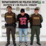 En la fotografía aparece un hombre capturado, acompañado de dos uniformados de la Policía Nacional. En la parte posterior un banner con logos de la entidad.