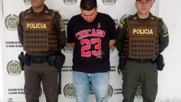 En la fotografía aparece un hombre capturado, acompañado de dos uniformados de la Policía Nacional. En la parte posterior un banner con logos de la entidad.