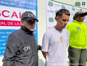 En la fotografía se aprecia de pie y con los brazos atrás a Juan Ángel Gómez Chavarro. Viste camiseta de manga corta blanca con estampado a la altura del pecho de una mano empuñando billetes. Al lado derecho de él hay un servidor del CTI de la Fiscalía y a su izquierda una uniformada de la Policía Nacional. Detrás de ellos hay dos pendones institucionales de la Fiscalía y la Policía.