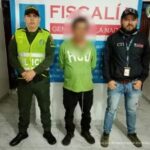 en la imagen se ve una persona detenida bajo cutodia de un investigador del CTI y de la Policía Nacional. detrás suyo un backing de la Fiscalía.