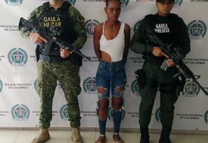 En la foto aparece de pie y con los brazos atrás, María Aura Cortés Quiñones. Viste una blusa blanca tipo body, sin mangas; jean azul con desgaste y sandalias. A lado y lado de ella hay uniformados de la Policía Nacional del Grupo Gaula. Detrás de ellos hay un pendón institucional de la Policía.