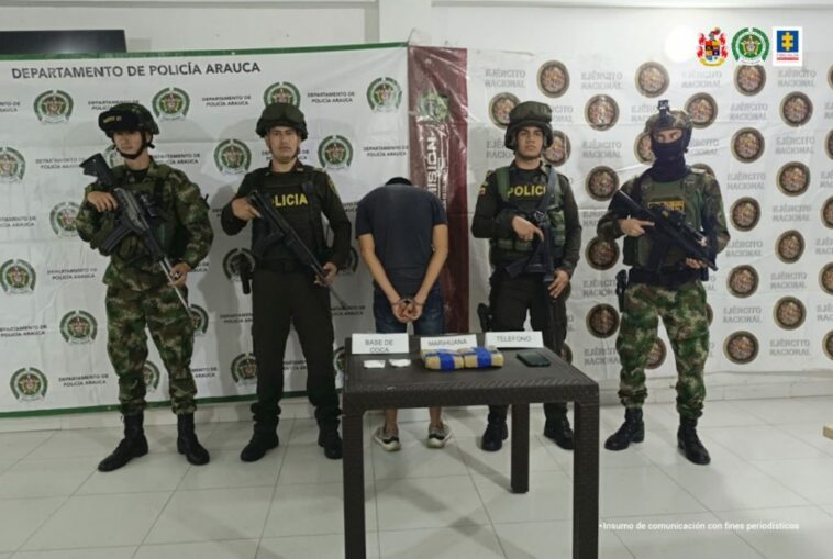 En la imagen se aprecia al capturado de espaldas junto a uniformados de la Policia y Ejército Nacional. Detrás de ellos banners que identifican al Departamento de Policía Arauca y Ejército Nacional.