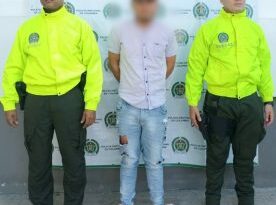 En la imagen se ve una persona detenida bajo custodia de dos integrantes de la Policía Nacional.