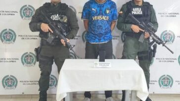 En la fotografía aparece Nick Kevin Tenorio Prado junto a dos agentes del Gaula de la Policía Nacional. En la parte posterior está una mesa con un teléfono celular