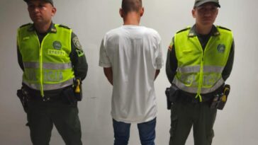 en la imagen se ve una persona detenida de espaldas bajo custodia de dos uniformados de la Policía Nacional.