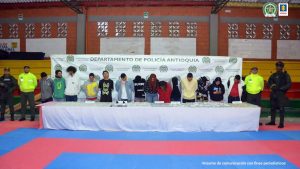 En la imagen están los 14 mayores de edad procesados con una mesa que contiene los elementos incautados y en ambos  lados 2 uniformados de la Policía Nacional