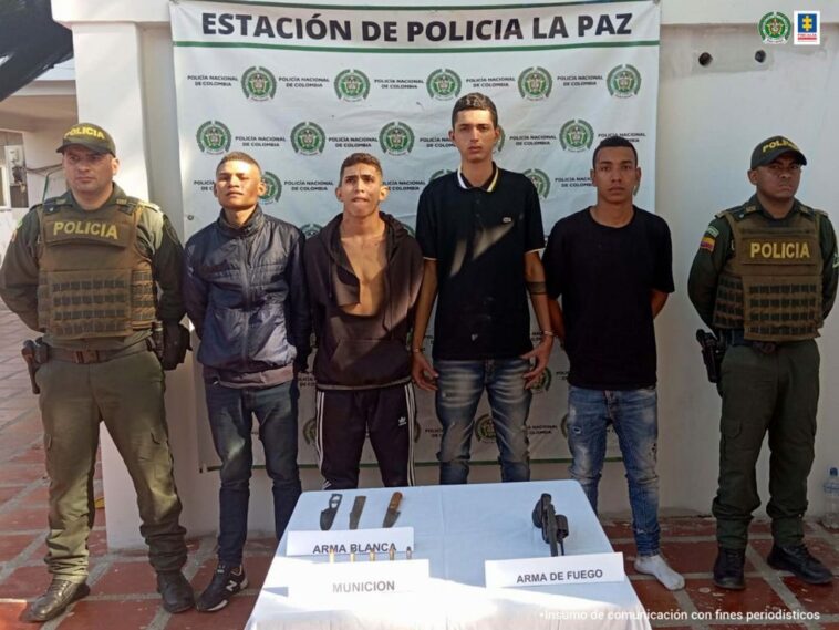 En la fotografía aparecen cuatro personas capturadas, acompañadas de dos uniformados de la Policía Nacional. En la parte posterior un banner con logos de la entidad.
