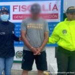 En la gráfica aparece el capturado junto a una investigadora del CTI y una uniformada de la Policía Nacional. Detrás de ellos el banner que identifica a la Fiscalía General de la Nación.