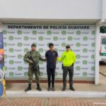 capturado de frentes masno atrás esposado cvustodiado por un militar y un policía. a los lados y dertrás banner de la Policía y del Ejército Nacional.