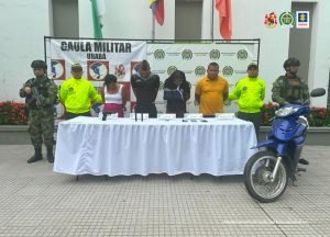 En la fotografía se encuentran los dos hombres y las dos mujeres capturadas, con un servidor de la Policía y otro del Ejército Nacional a cada lado, con una mesa en la que están las armas de fuego y los elementos incaurados.