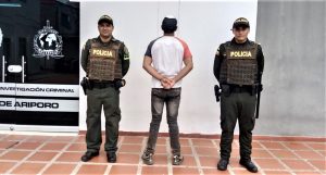 El capturado está rodeado por dos uniformados de la policía nacional y de espalda a la cámara.