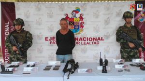 En la fotografía aparece el capturado junto a uniformados del Ejército Nacional. Frente a ellos se ubica una mesa con el  material incautado: armas, municiones, proveedores,  radios de comunicación y  teléfonos celulares.