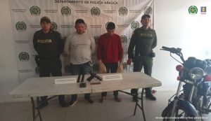 En la imagen se observa a los dos capturados junto a uniformados de la Policía Nacional. En parte posterior se visualiza el banner que identifica al Departamento de Policía de Arauca.