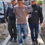 En la fotografía se aprecia a Héctor Favio Medina Ospina, en acción de caminata, en una vía pública, con los brazos atrás. Viste camiseta de manga corta color claro, jean azul desgastado y tenis blancos. Al lado izquierdo de él hay un servidor del CTI de la Fiscalía y al lado derecho un uniformado de la Policía Nacional