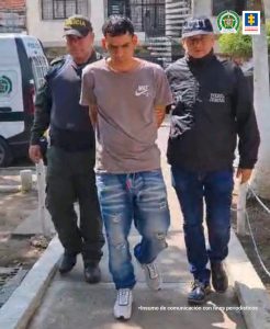 En la fotografía se aprecia a Héctor Favio Medina Ospina, en acción de caminata, en una vía pública, con los brazos atrás. Viste camiseta de manga corta color claro, jean azul desgastado y tenis blancos. Al lado izquierdo de él hay un servidor del CTI de la Fiscalía y al lado derecho un uniformado de la Policía Nacional