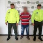 en la imagen se ve un hombre detenido bajo custodia de dos uniformados de la Policía Nacional. Detrás suyo un backing institucional.