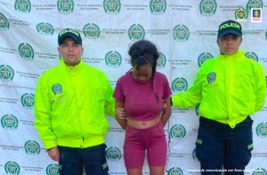 En la foto aparece Jeniffer Andrea Mosquera Córdoba con dos policías a los lados y atrás el pendón de la Policía Nacional.