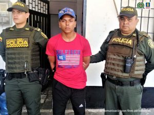 Los capturados están custodiados por uniformados de la policía nacional, esposados y con un pendón institucional detrás de ellos.