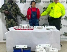 En la fotografía aparece la capturada junto a un agente de la Policía Nacional y un soldado del Ejército. En la parte posterior está una mesa con detonadores, morfina y dinero en efectivo. En el piso están siete carretes de cordón detonante.