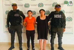 En la fotografía aparecen dos mujeres capturadas, acompañadas de dos uniformados de la Policía Nacional. En la parte posterior un banner con logos de la entidad.
