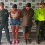 en la imagen se ve un hombre y una mujer detenidos bajo custodia de dos integrantes de la Policía Nacional. Detrás suyo un backing institucional.