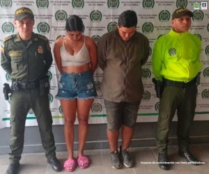 en la imagen se ve un hombre y una mujer detenidos bajo custodia de dos integrantes de la Policía Nacional. Detrás suyo un backing institucional.