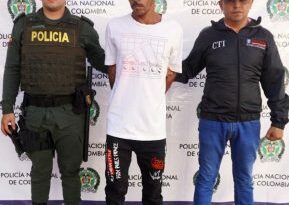 El capturado tiene una camiseta blanca, gorra y está custodiado por un servidor del CTI de la Fiscalía y un uniformado de la Policía Nacional.