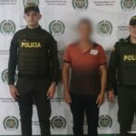En la imagen se visualiza al capturado de espalda junto a dos uniformados de la Policía Nacional. En la parte posterior se observa el banner que identifica a la Policía Nacional del departamento de Arauca.