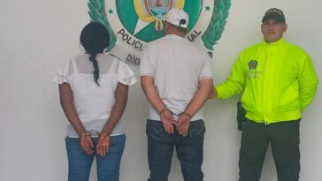En la fotografía están los dos investigados de espalda con un uniformado de la Policía Nacional y un pendón de esa institución.