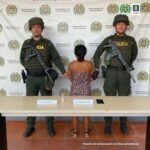 En la fotografía se aprecia a la capturada de espaldas junto a dos uniformados de la Policía Nacional. Frente a ellos una mesa con el equipo celular incautado. Detrás de ellos el banner que identifica al Departamento de Policía de Arauca.