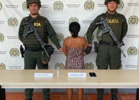 En la fotografía se aprecia a la capturada de espaldas junto a dos uniformados de la Policía Nacional. Frente a ellos una mesa con el equipo celular incautado. Detrás de ellos el banner que identifica al Departamento de Policía de Arauca.