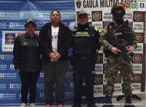 En la fotografía aparece la detenida junto a un servidor del CTI, un agente de la Policía Nacional y un soldado del Gaula Militar. En la parte superior está un banner de la Fiscalía General y otro banner del Gaula Militar