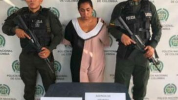 En la fotografía aparece una mujer capturada, acompañada de dos uniformados de la Policía Nacional. En la parte posterior un banner con  logos de la entidad.