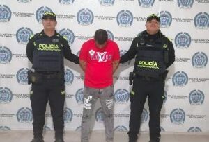 En la fotografía aparece una persona capturada, acompañado de dos uniformados de La Policía. En la parte posterior un banner con logos de la entidad.